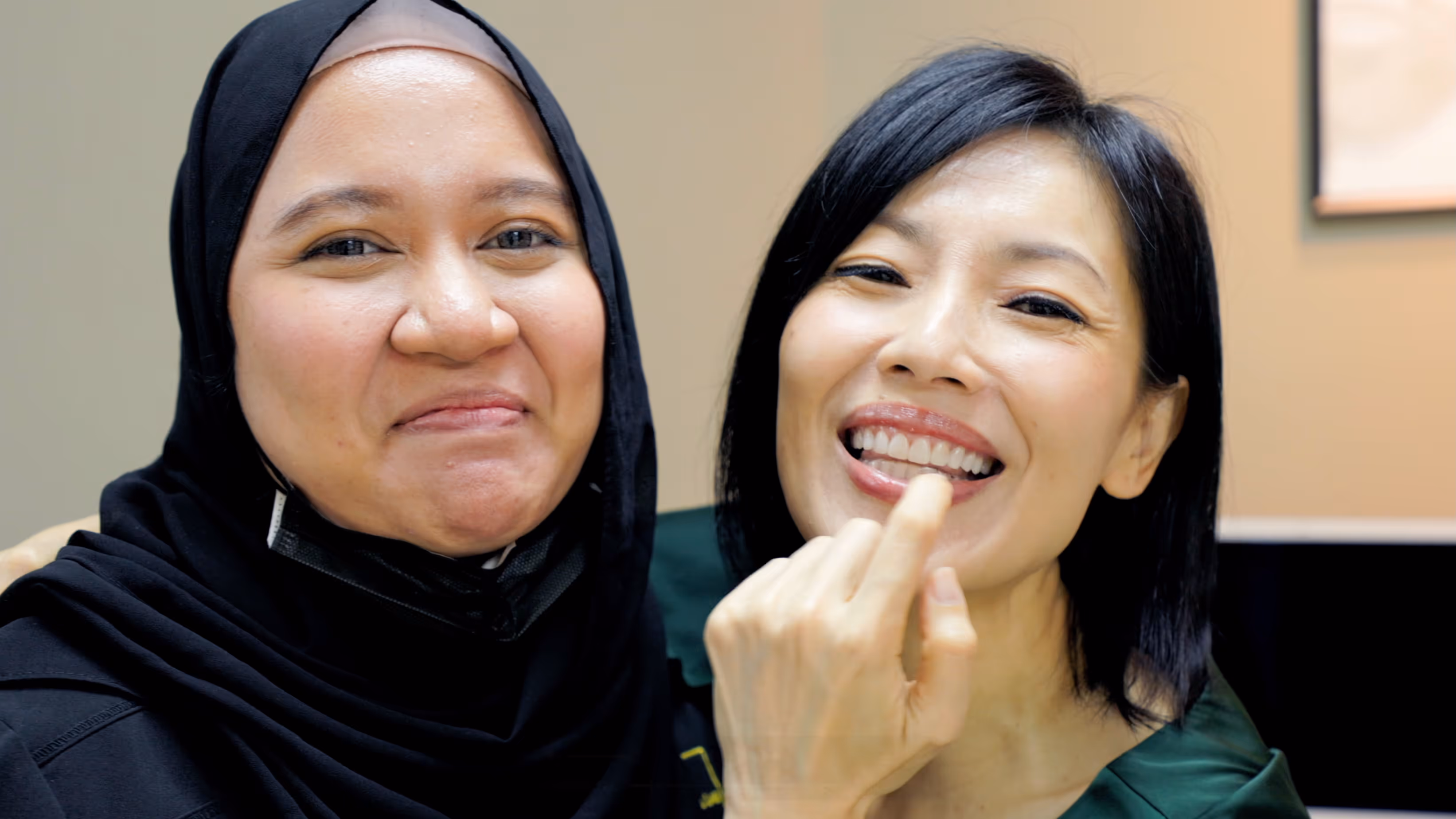 Sharon Au with Fatima her ceramist smiling; one wearing a black hijab and the other with short black hair touching her smiling teeth.