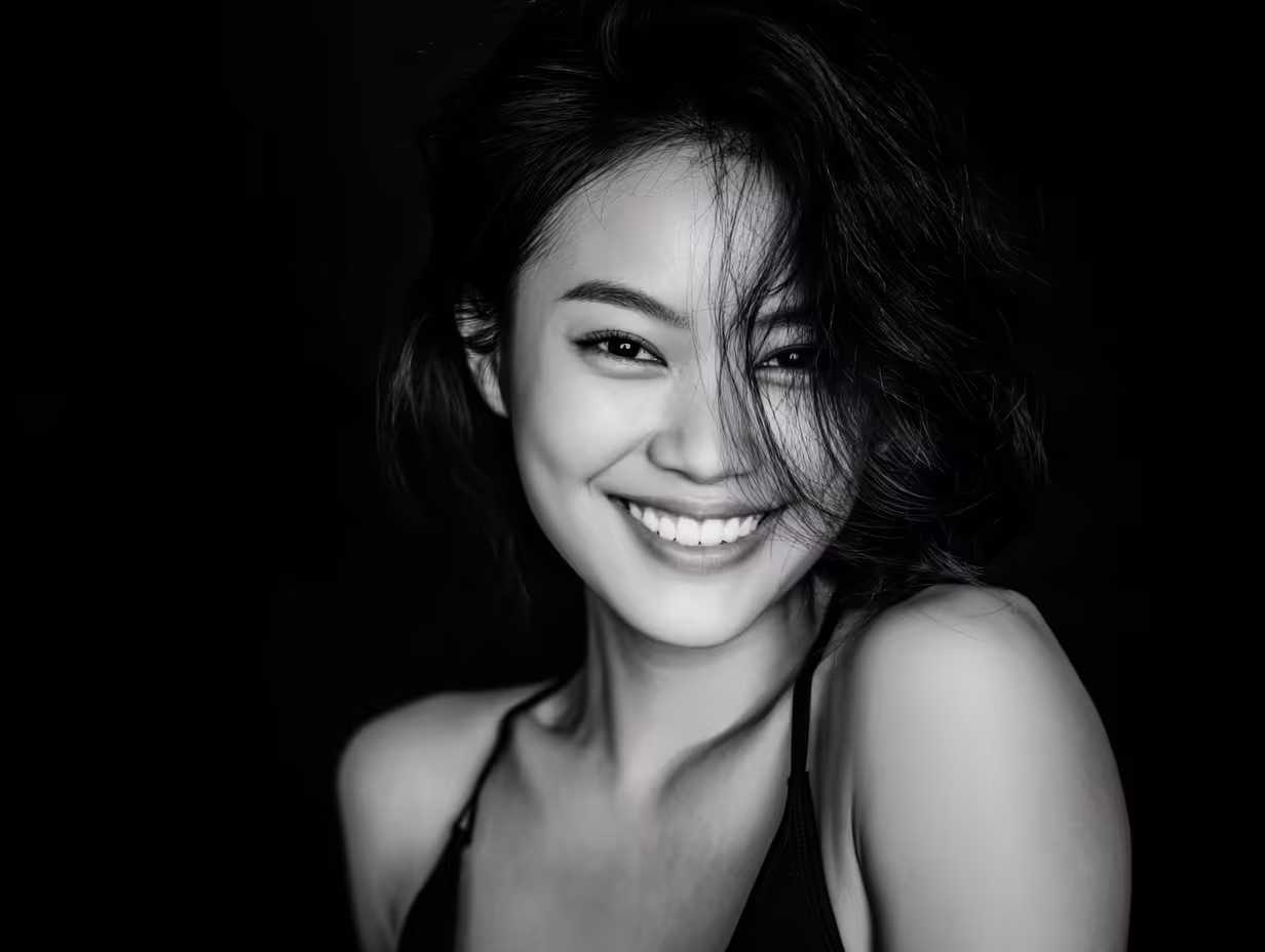 Close-up black and white portrait of a smiling woman with tousled hair against a dark background.