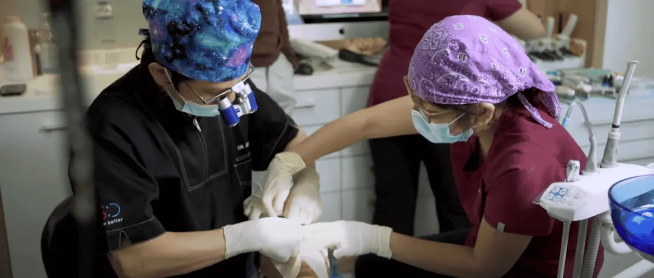 Dr. Jerry Lim with dental professionals wearing surgical masks and caps performing a dental procedure on a patient in a clinic.