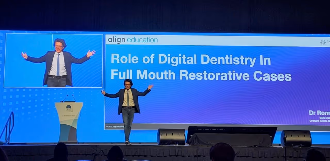 Dr. Ronnie on stage gesturing with arms open during a presentation titled 'Role of Digital Dentistry in Full Mouth Restorative Cases'.