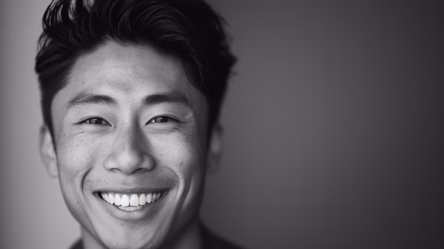 Smiling young Asian man with short hair against a plain background in black and white.