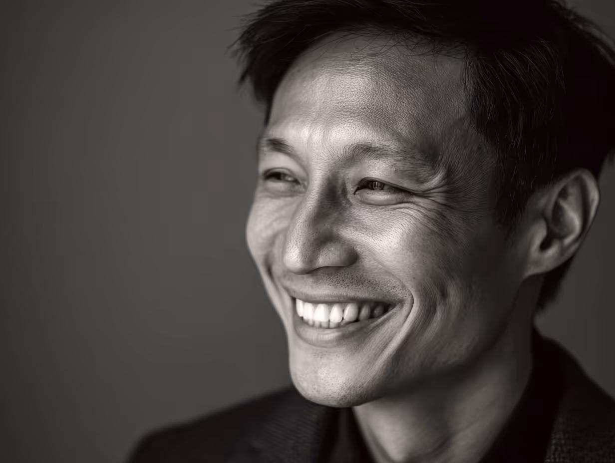Black and white close-up portrait of a smiling man looking to the side.
