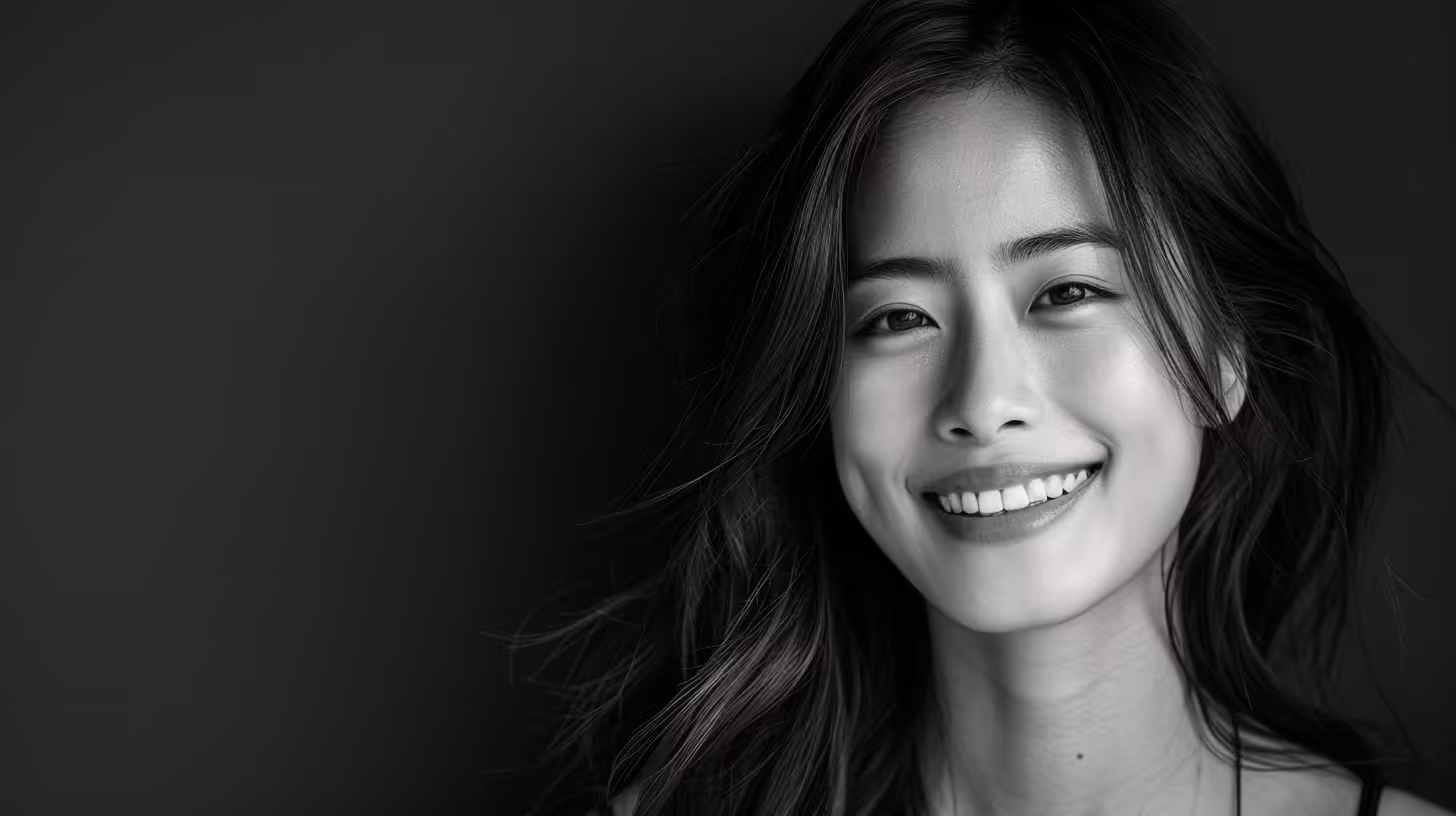 Close-up portrait of a young Asian woman smiling against a dark background.