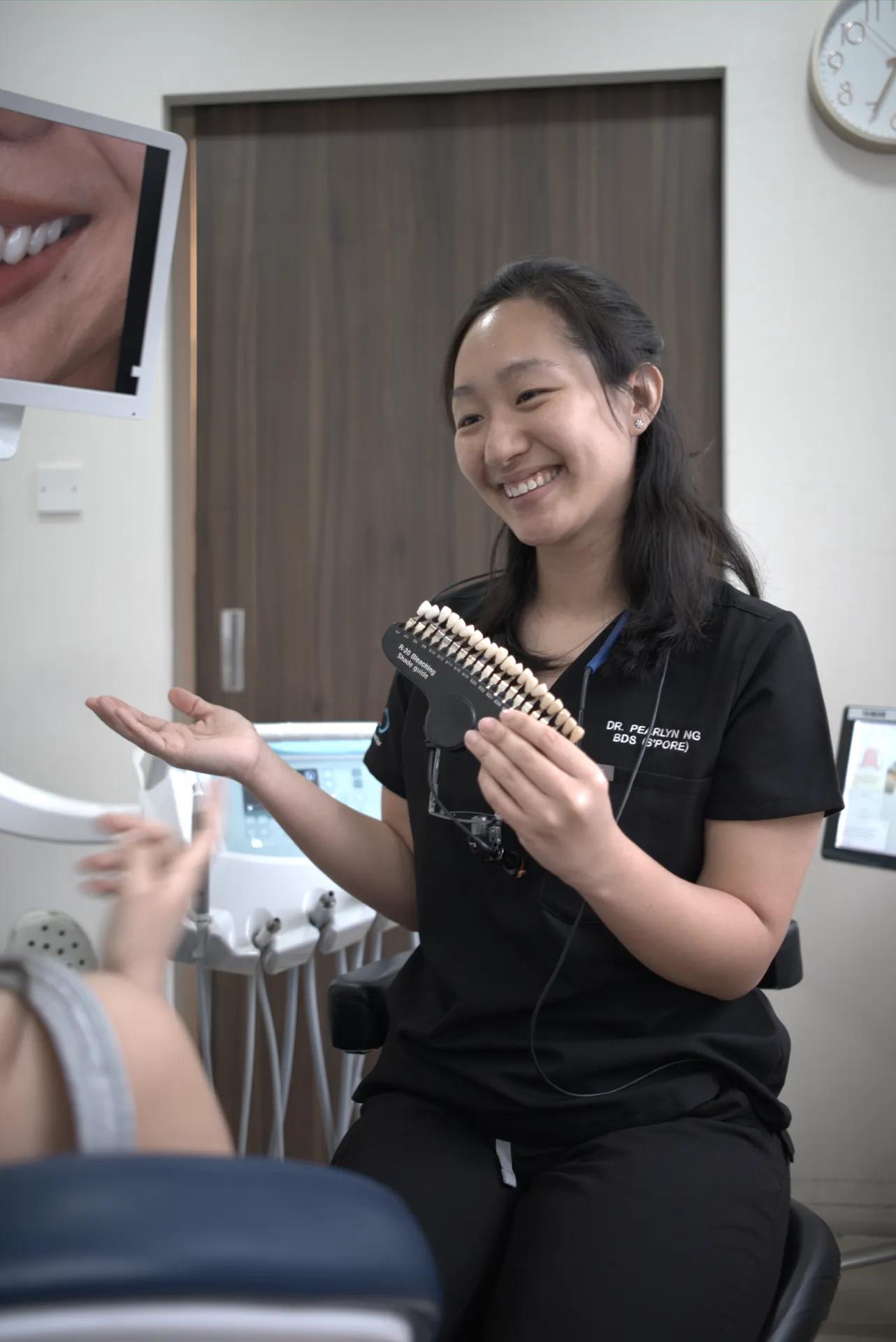 Dr Pearlyn Ng smiling as she holds a tooth-shade guide during a patient consultation at Orchard Scotts Dental